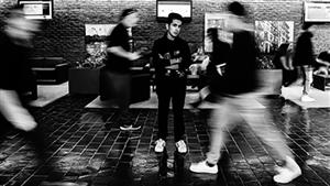 Student stands fixated and surrounded by bodies blurred in motion 